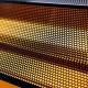 Close-up de uma grade metálica perfurada com iluminação amarela intensa ao fundo.