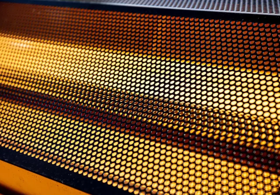 Close-up de uma grade metálica perfurada com iluminação amarela intensa ao fundo.