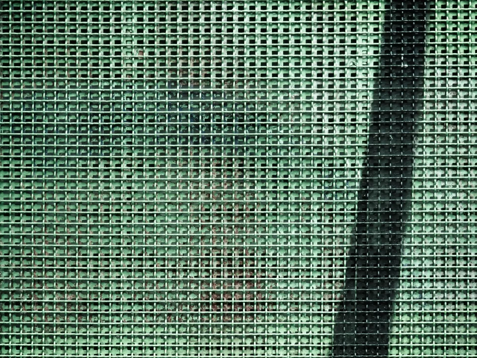 Close-up de uma grade metálica verde com sombra projetada sobre a superfície.