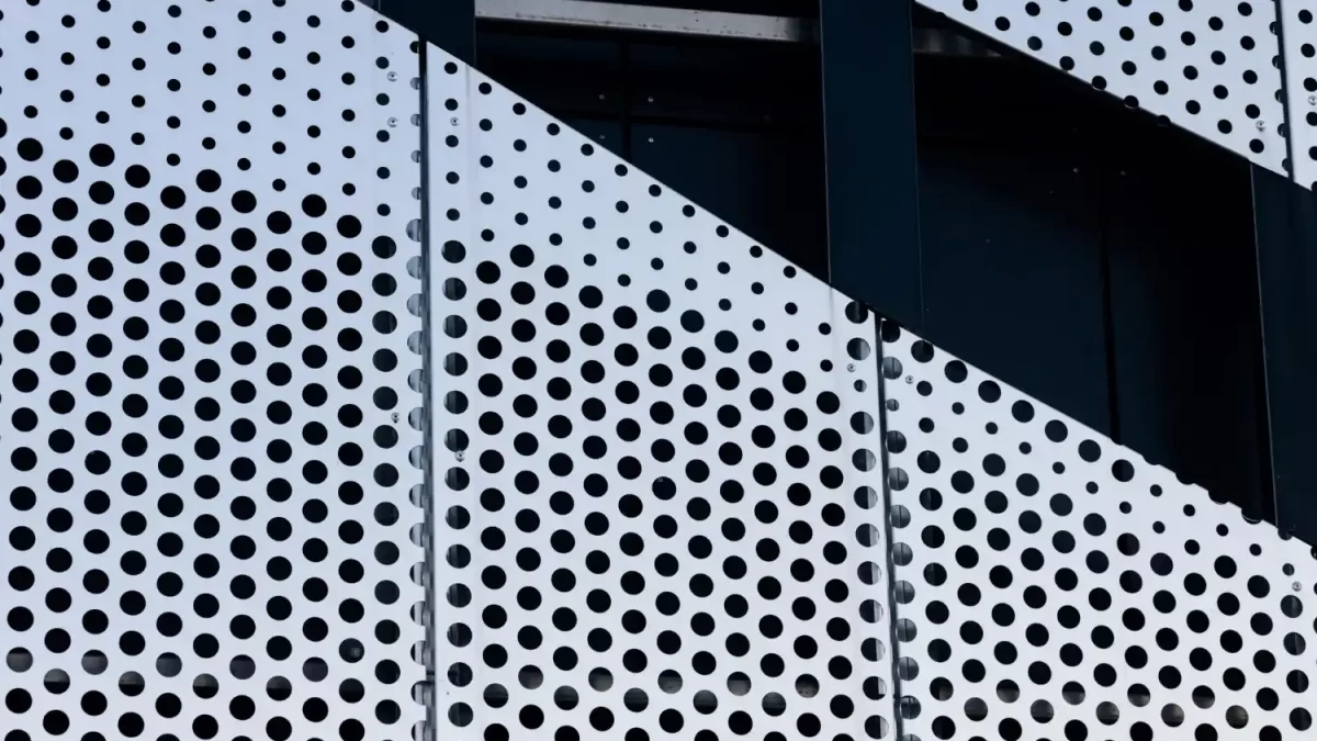 Textura de telas de metal perfuradas em um prédio, com painéis brancos e furos pretos.