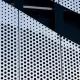 Textura de telas de metal perfuradas em um prédio, com painéis brancos e furos pretos.