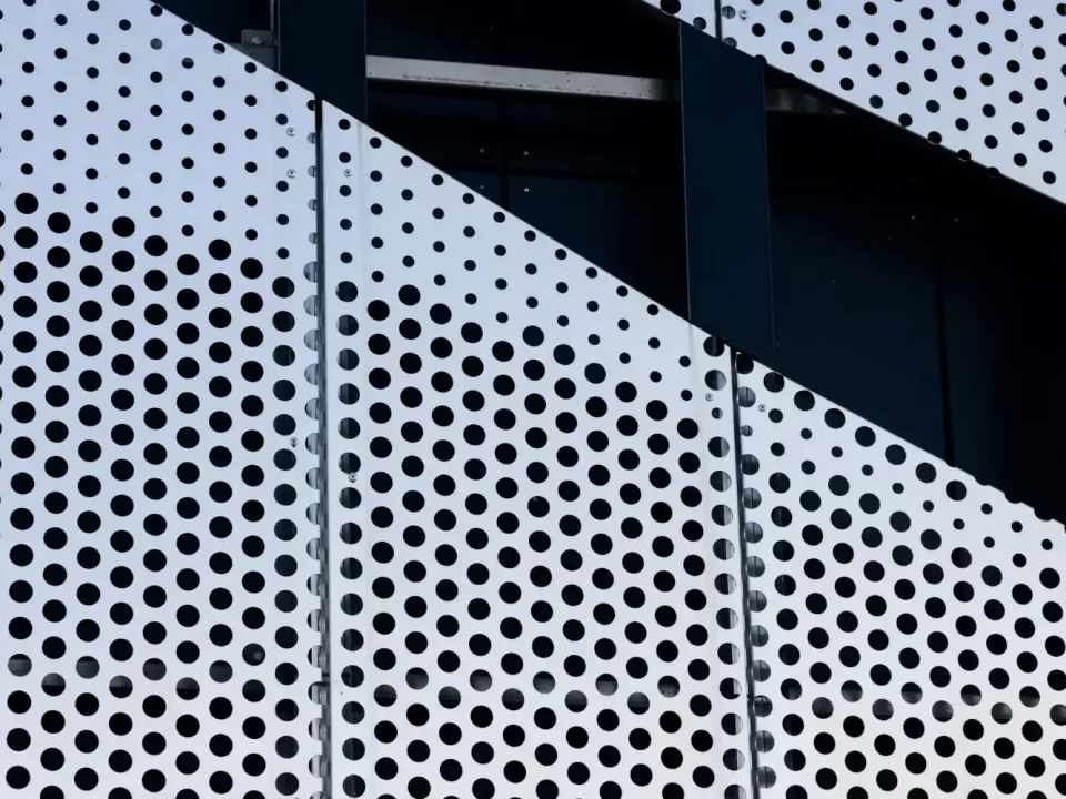 Textura de telas de metal perfuradas em um prédio, com painéis brancos e furos pretos.