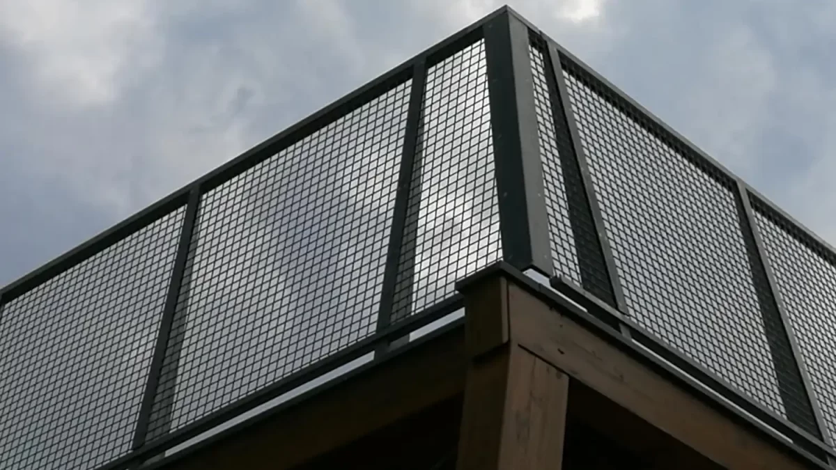 Guarda-corpo metálico com tela perfurada quadrada, usado como proteção e composição arquitetônica em estrutura elevada.