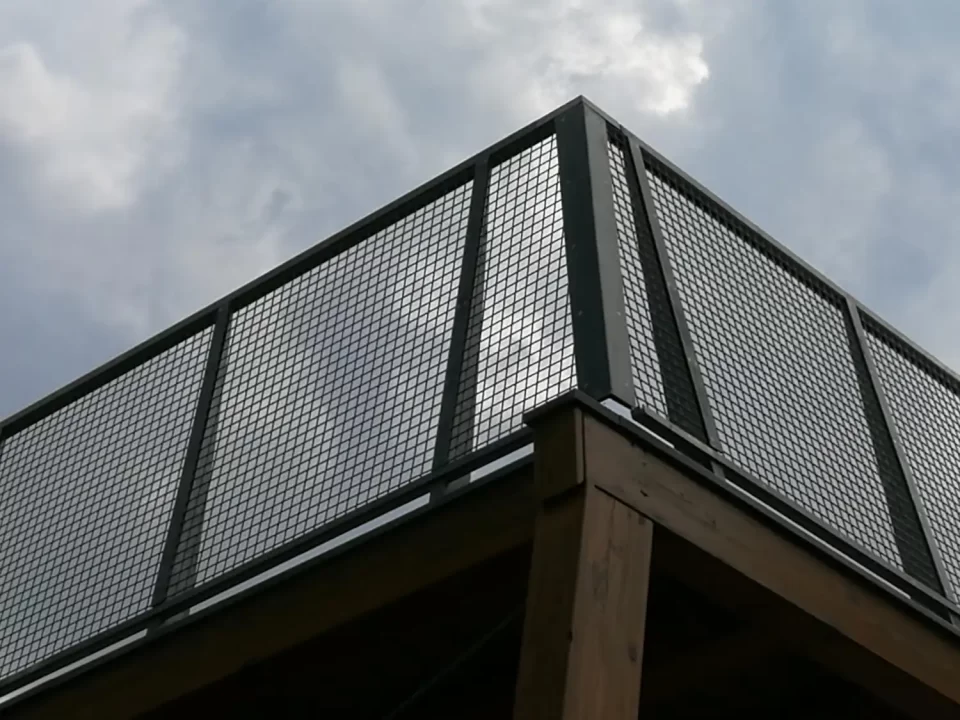 Guarda-corpo metálico com tela perfurada quadrada, usado como proteção e composição arquitetônica em estrutura elevada.